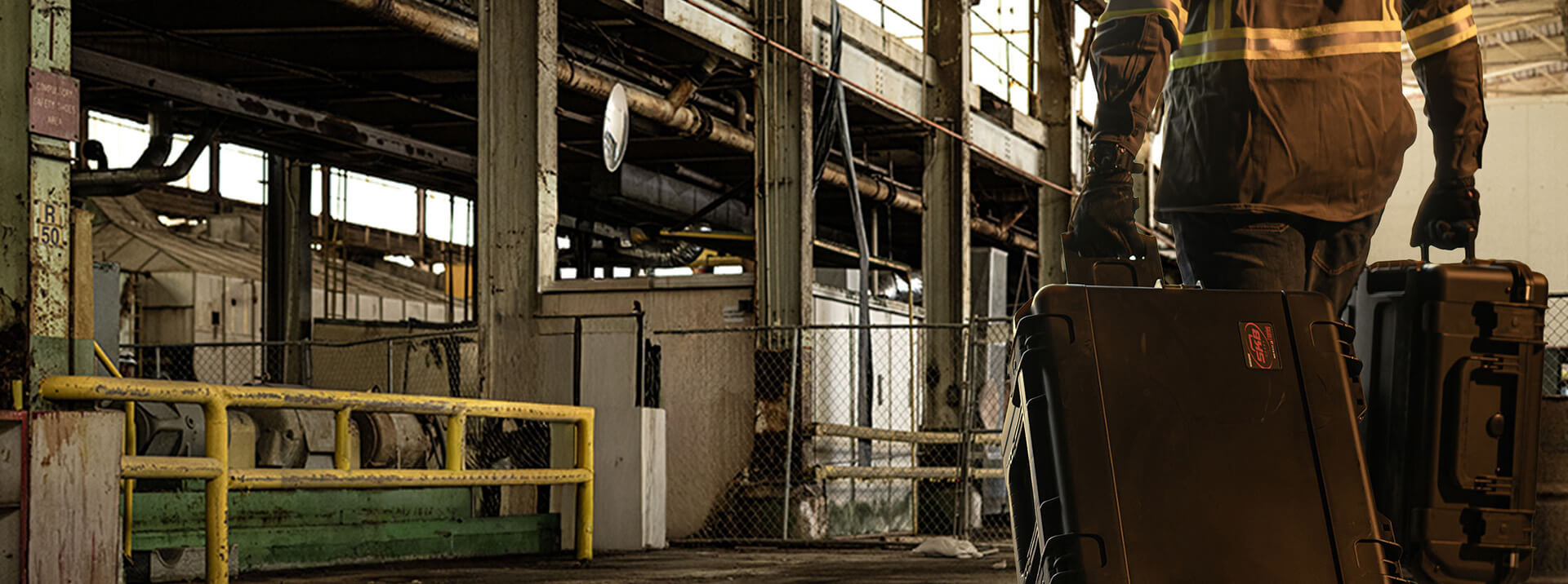 Person in a high-visibility jacket walking through an industrial setting with large equipment.
