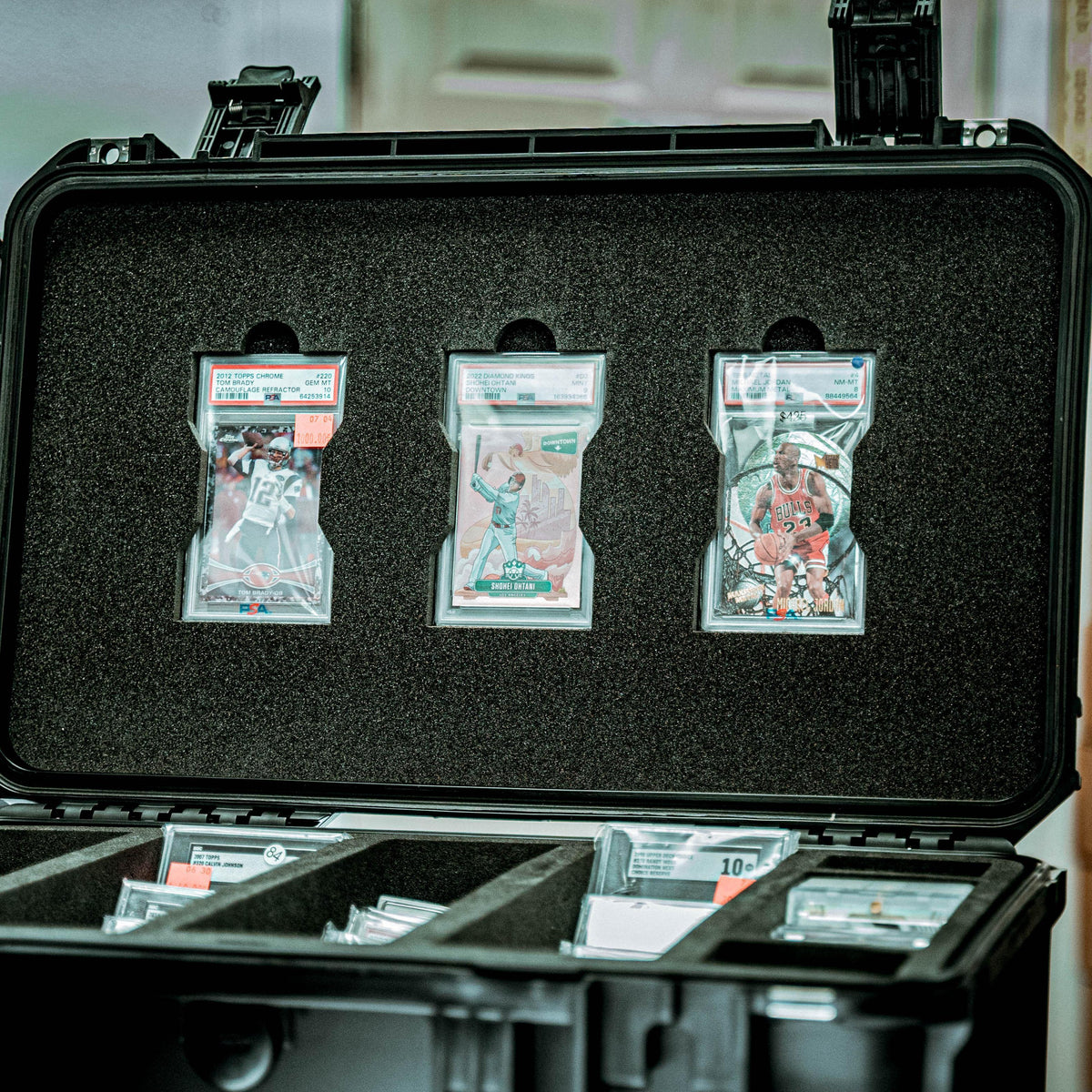 Open black protective case with foam compartments holding several PSA-graded card sleeves on a dark textured insert.