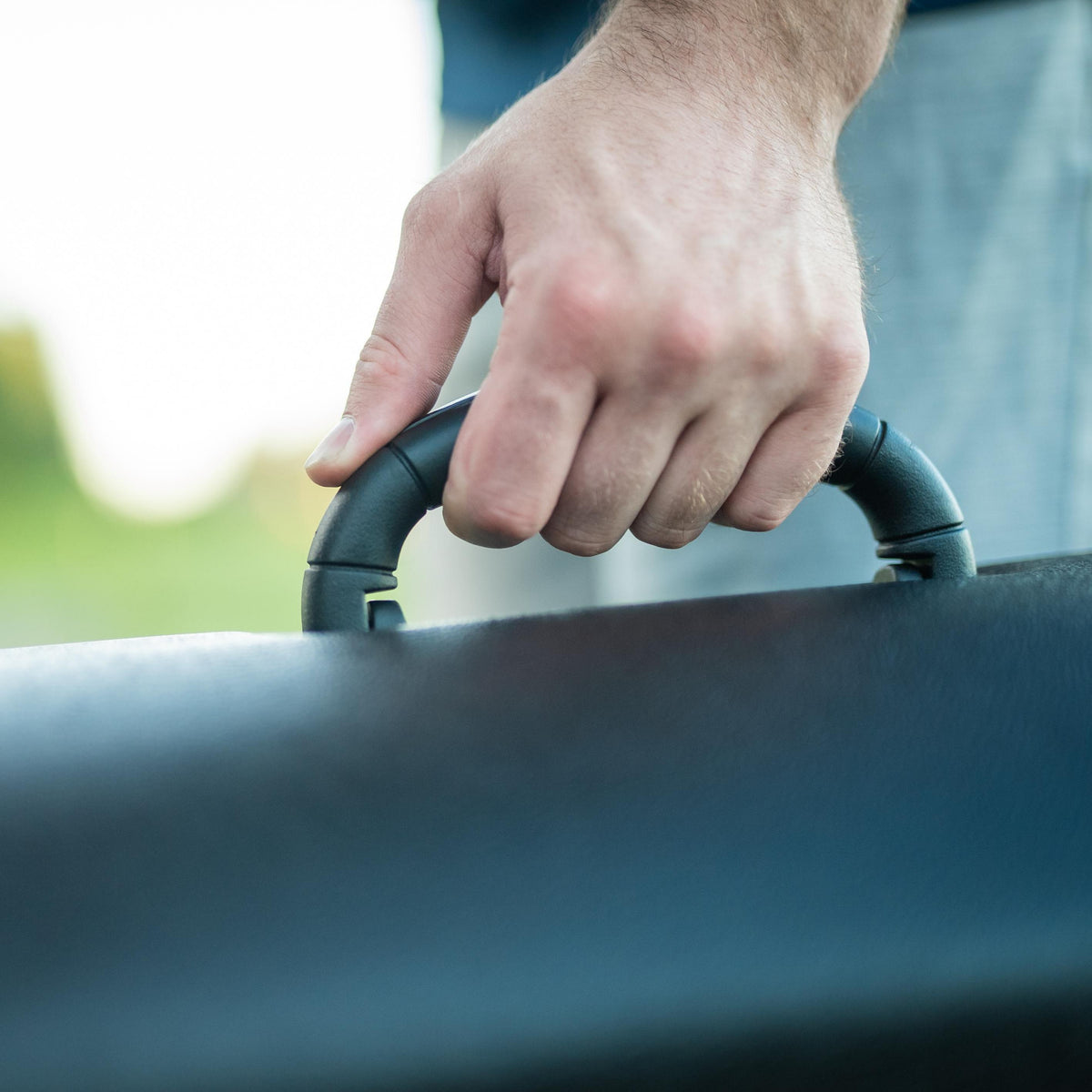 A close-up of a person's hand gripping the handle of a dark blue-gray briefcase or hard carrying case.