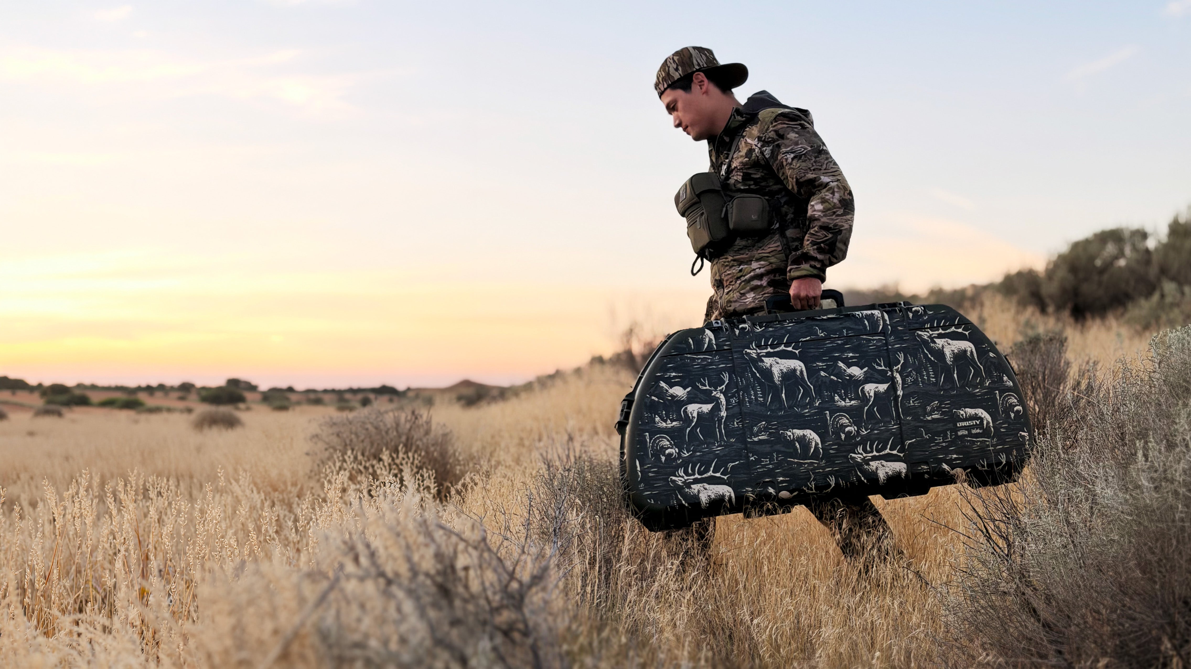 Man in a black jacket and baseball cap standing outdoors with an SKB bow case.