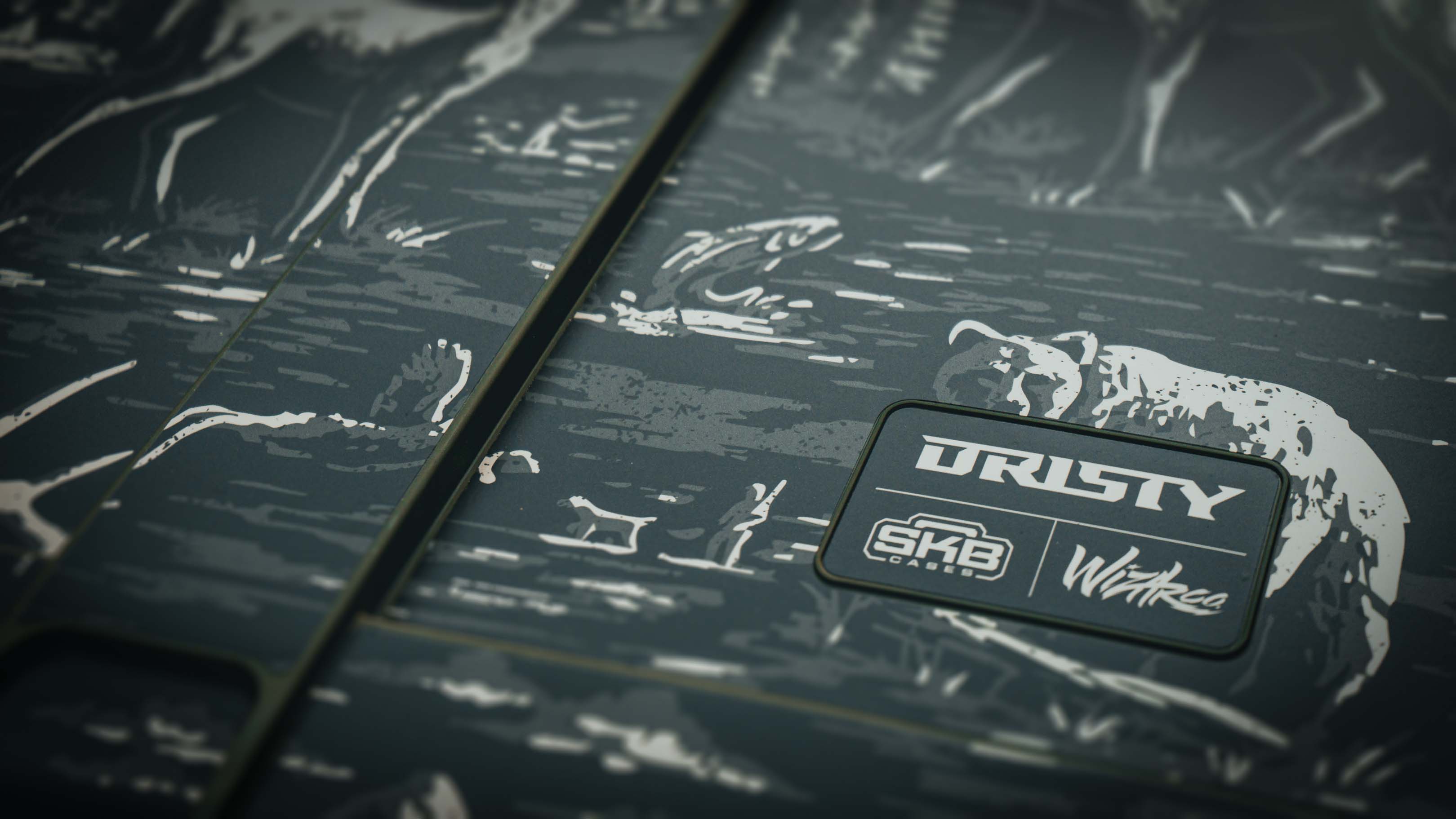 Close-up angled shot of an olive green SKB hard case featuring etched wildlife artwork of a bear and turkey surrounding a branded rubber patch with Dristy, SKB Cases, and Wildear logos.