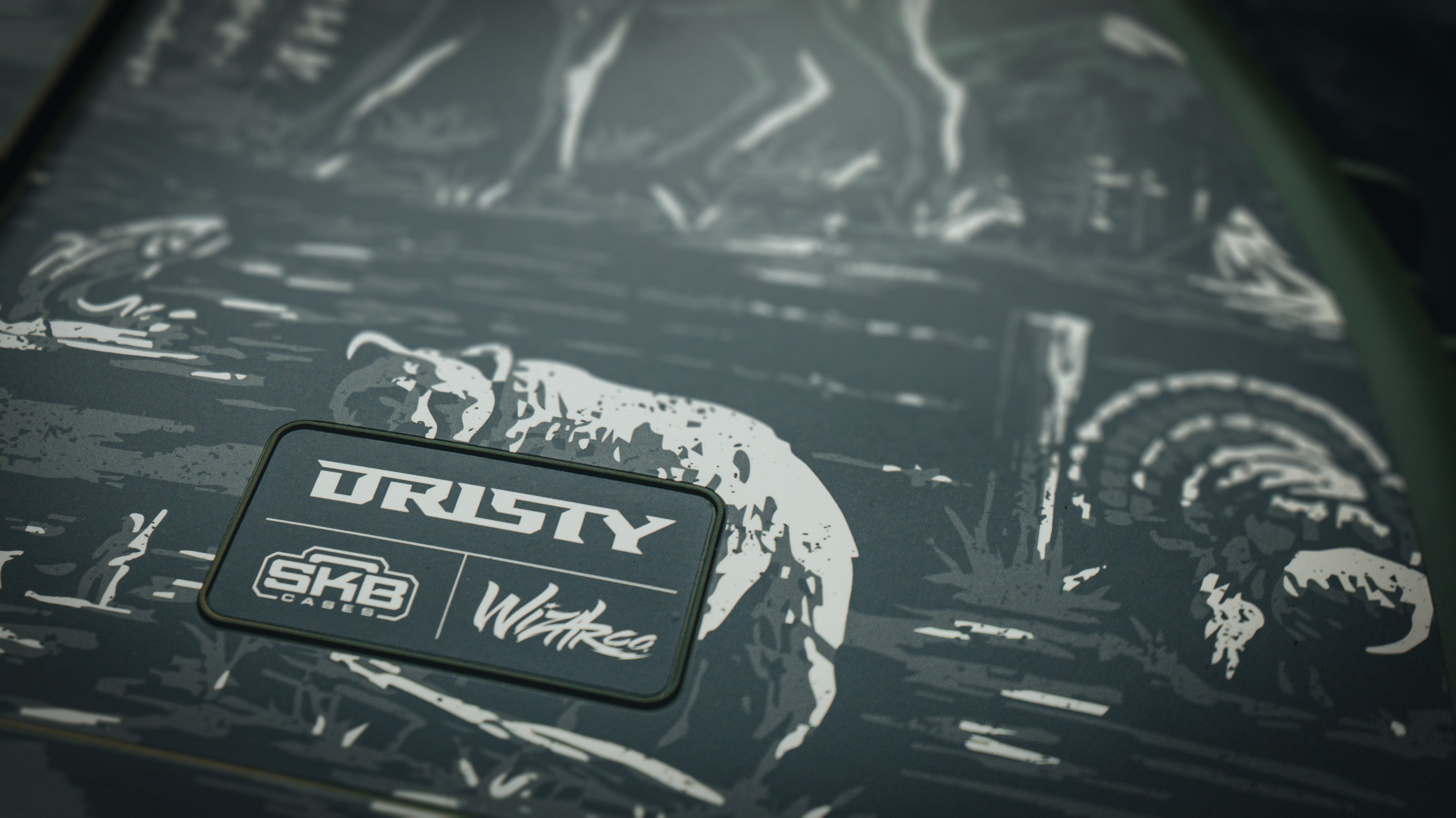 Close-up angled shot of an olive green SKB hard case featuring etched wildlife artwork of a bear and turkey surrounding a branded rubber patch with Dristy, SKB Cases, and Wildear logos.