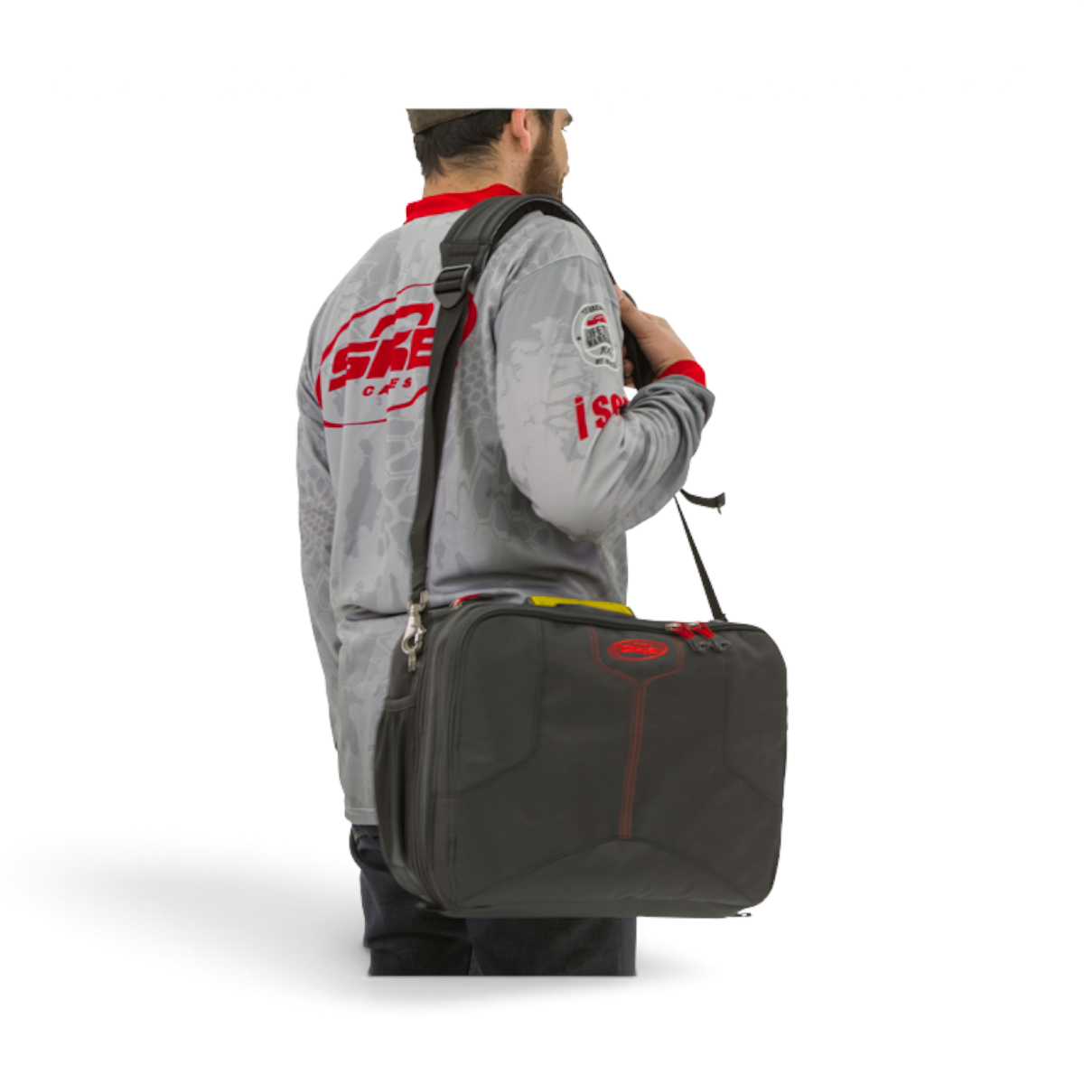 A man wearing a grey SKB Cases long-sleeve shirt carries a black iSeries 1309-6 waterproof lure case with a shoulder strap.